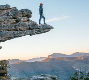 A man with a side hustle standing on top of a cliff in the blue mountains.