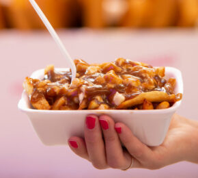 A person holding a bowl of fries and gravy, showcasing the best poutine in Montreal.