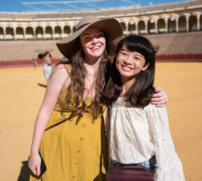 Two women solo traveling, posing in front of an arena.