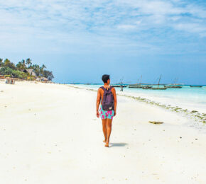 A woman walking on a white sandy beach in Tanzania.