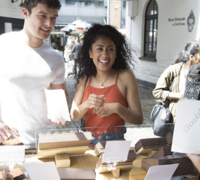 A man and a woman looking at chocolates at a street food stall.