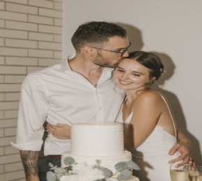 A real love story unfolds as the bride and groom share a tender kiss in front of their exquisite wedding cake.