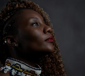 A woman with curly hair is looking up at a vibrant LGBTQIA+ travel poster against a dark background.