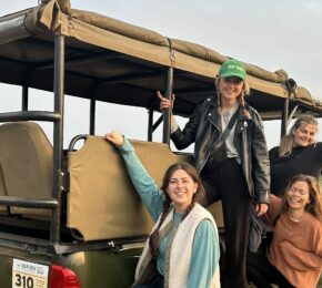 Four women on a trip to South Africa posing on the back of a safari vehicle.