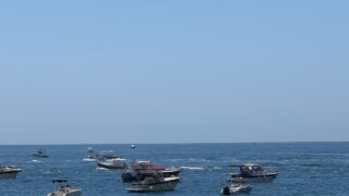 Green and yellow patio umbrellas with boats in the sea in the background