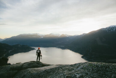 One of the best places to travel alone - a person standing on top of a mountain overlooking a lake.