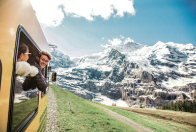 Two young travellers riding a train through alps