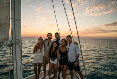 Young people standing on sailboat foredeck at sunset