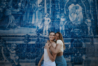 Two women hugging during their travel adventure in front of a blue tiled wall.