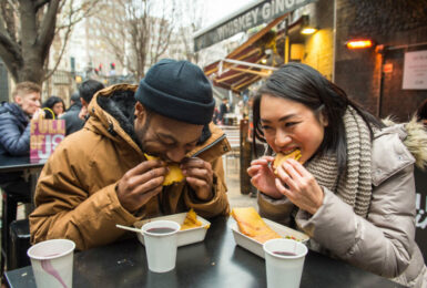 Two people enjoying food at an outdoor table at a food festival.