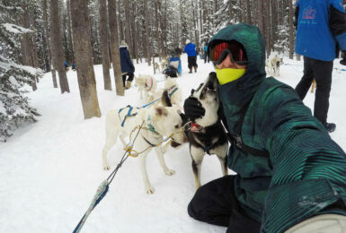 A man is taking a selfie with a group of huskies.