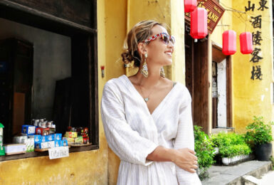 A woman in a white dress standing in front of a building showcasing Hoi An fashion.