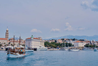 A boat sailing near a city in Croatia with mountains in the background.