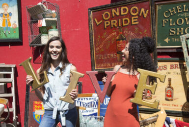 Two women holding signs at a flea market in the UK.