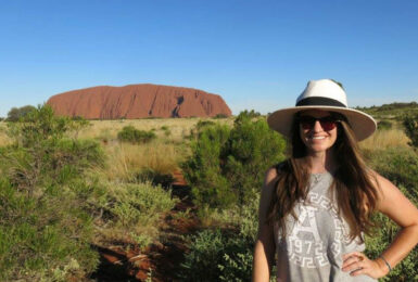 A woman in a hat traveling in front of Uluru.