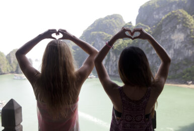 Two women using dating apps and making a heart shape with their hands.