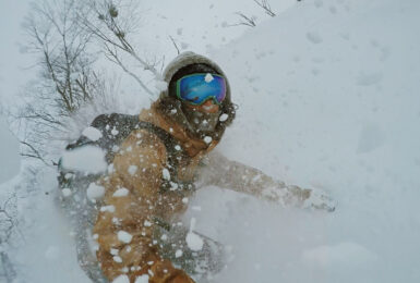 A person wearing goggles is snowboarding down a snowy slope in Asia.