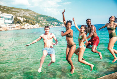 A group of young people diving into the water during their travel.