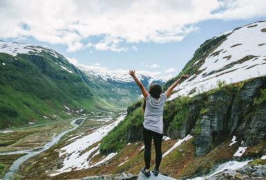 A woman standing on top of a mountain in the happiest country in the world with her arms raised.