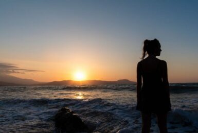 A silhouette of a woman standing on the beach at sunset.