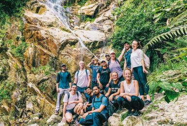 A group of people travelling and posing in front of a waterfall.