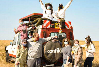 A group of people standing on top of a truck during an African safari experience in the middle of a field.