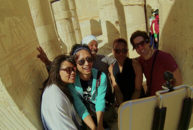 A group of people are posing for a photo in front of a ancient egyptian temple during their travels.