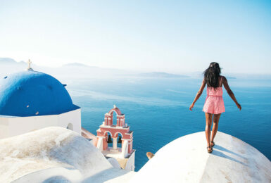 A woman is solo travelling on top of a hill overlooking the ocean.