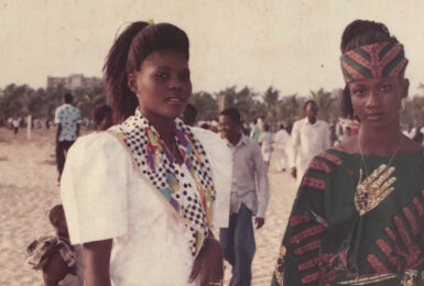 Two African women in traditional clothing standing on the beach.