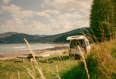 A camper van parked on a grassy hill next to the ocean.