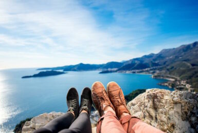 Two people using phone photography on top of a mountain overlooking the sea.