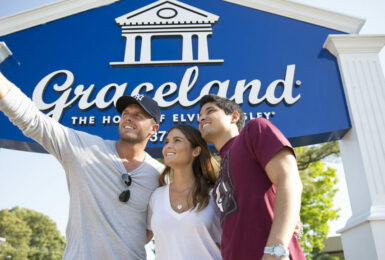Three people taking a picture in front of the Graceland sign, representing Tennessee's music history.