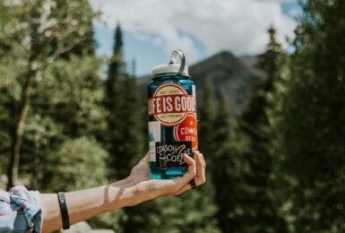 A person holding up a blue water bottle with sustainable travel tips in the background.