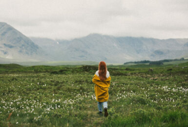 A woman walking through a field in Scotland with mountains in the background.