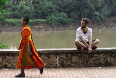 Two meditating monks sitting on a wall next to a river.