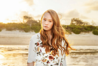 A girl in a floral dress standing on the beach at sunset, Madeline Stuart.