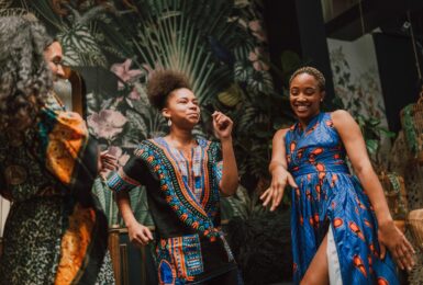 A group of African women dressed in colorful dresses dancing in a room.