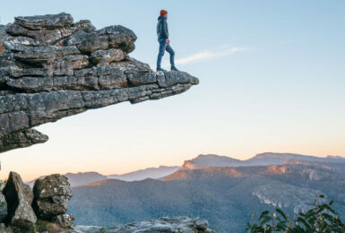 A man with a side hustle standing on top of a cliff in the blue mountains.