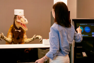 A woman is standing in front of a robot at a counter in a dinosaur-themed hotel.