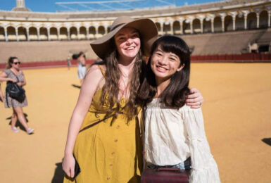 Two women solo traveling, posing in front of an arena.