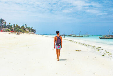 A woman walking on a white sandy beach in Tanzania.