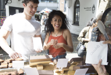 A man and a woman looking at chocolates at a street food stall.