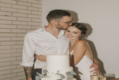 A real love story unfolds as the bride and groom share a tender kiss in front of their exquisite wedding cake.