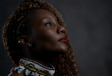 A woman with curly hair is looking up at a vibrant LGBTQIA+ travel poster against a dark background.