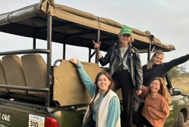 Four women on a trip to South Africa posing on the back of a safari vehicle.