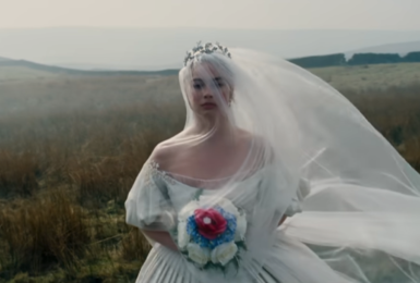 Margot Robbie in field carrying bouquet and dressed in white wedding gown in Wuthering Heights