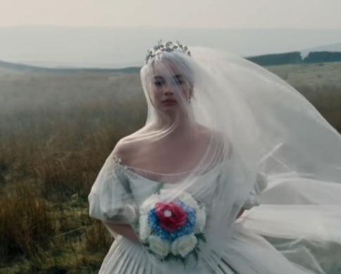 Margot Robbie in field carrying bouquet and dressed in white wedding gown in Wuthering Heights