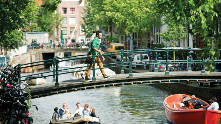 Young people crossing a bridge over a canal in Amsterdam, Netherlands.