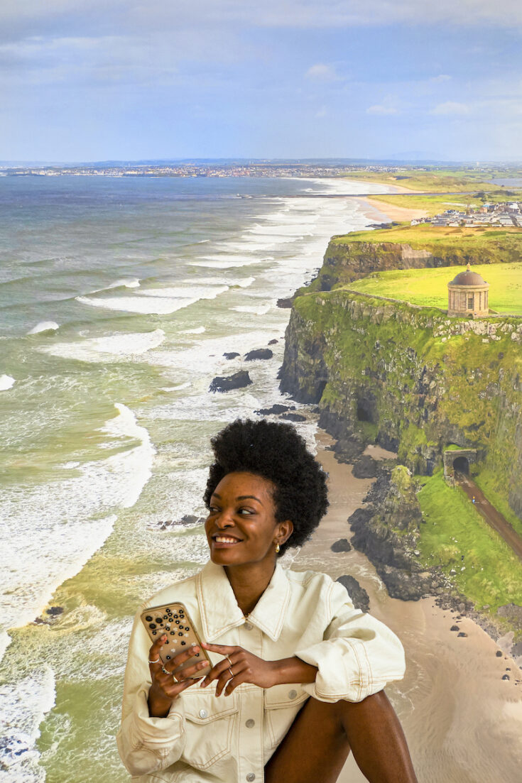 Young woman sitting with coastline in Northern Ireland as the background.