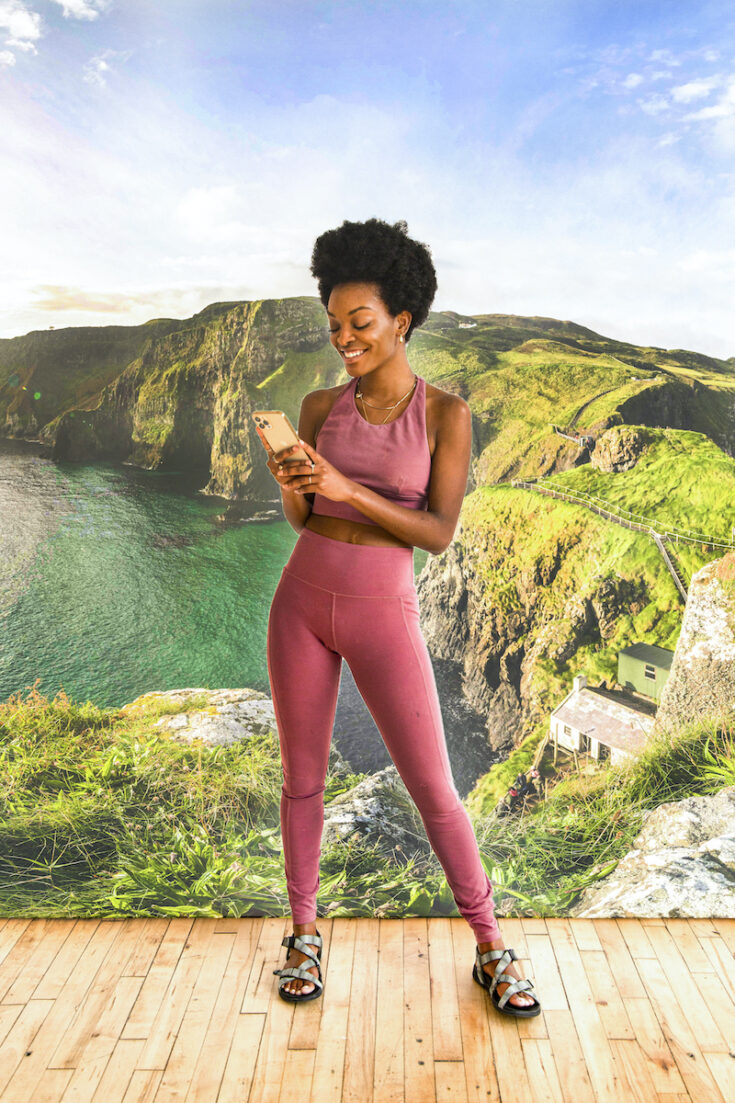 Young woman using her mobile phone with hills and sea in Northern Ireland as the background.